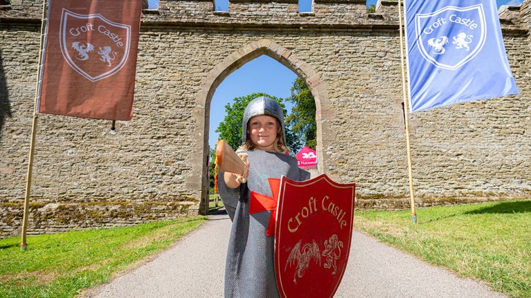 A child holding a toy sword and shield in front of the Gothic Arch at Croft Castle